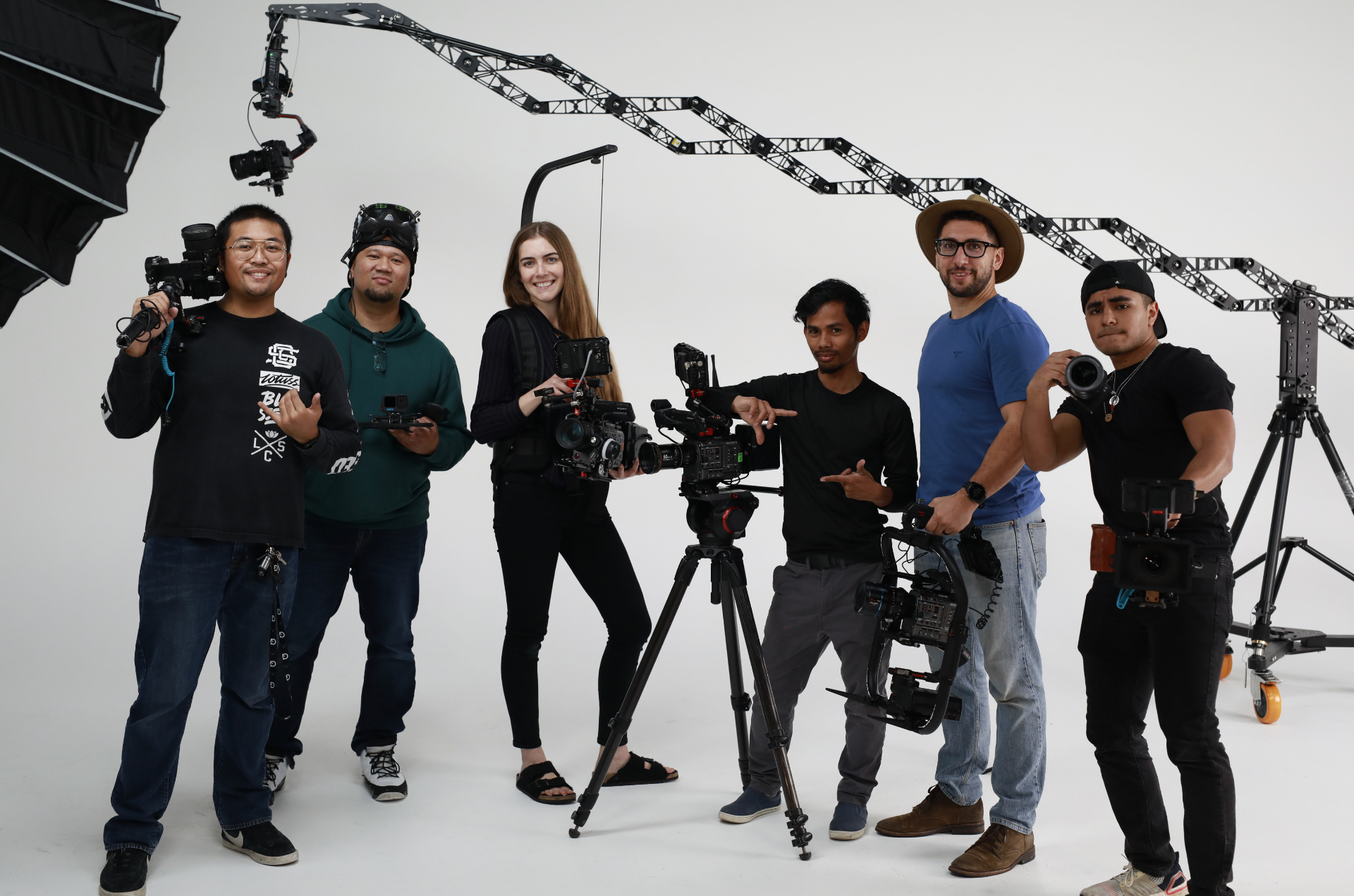 A production crew posed together in a bright studio with cinema cameras, gimbals, and an overhead truss rig.