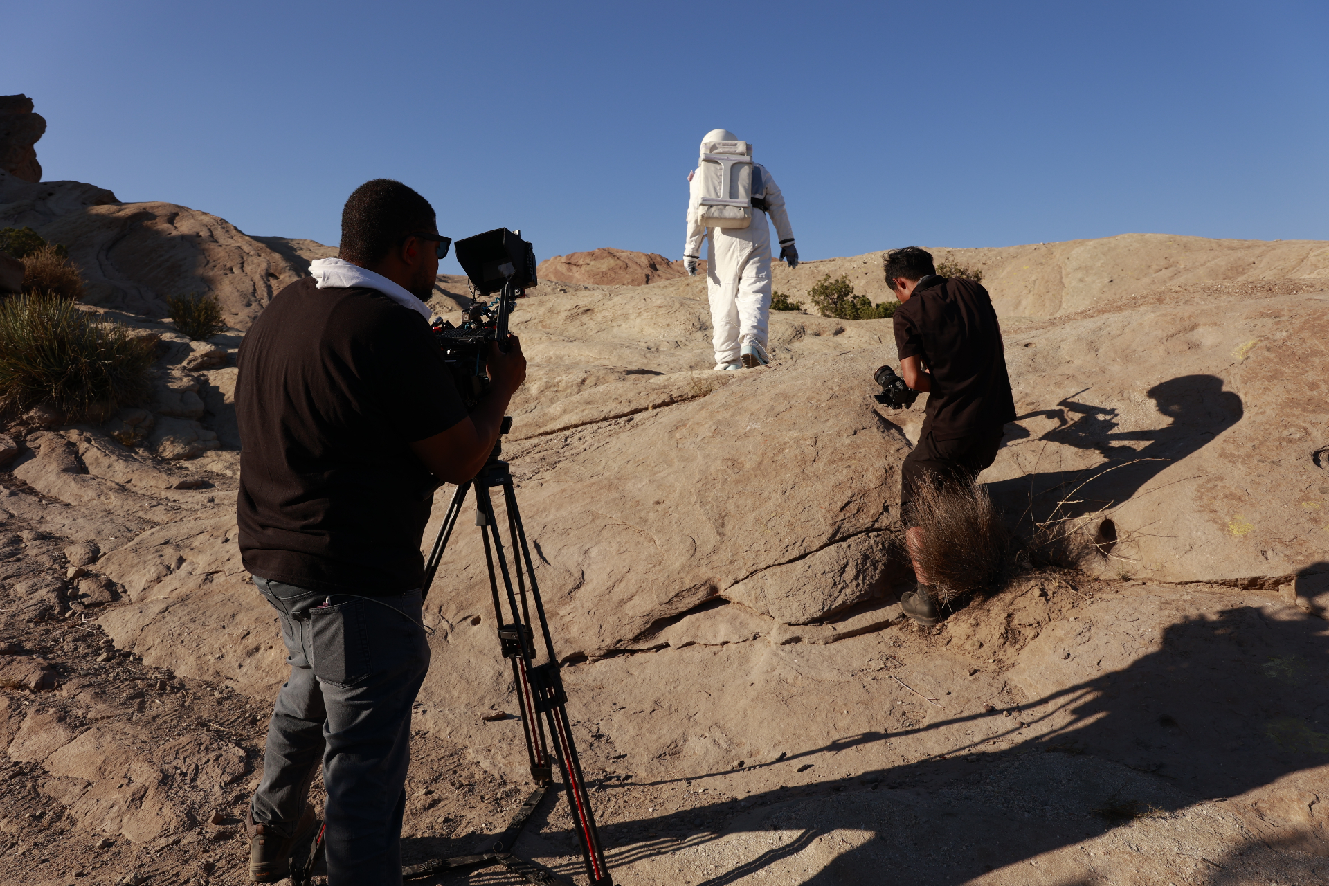 Leomar Moring and crew filming on location in a desert landscape with an astronaut-like figure in the distance.