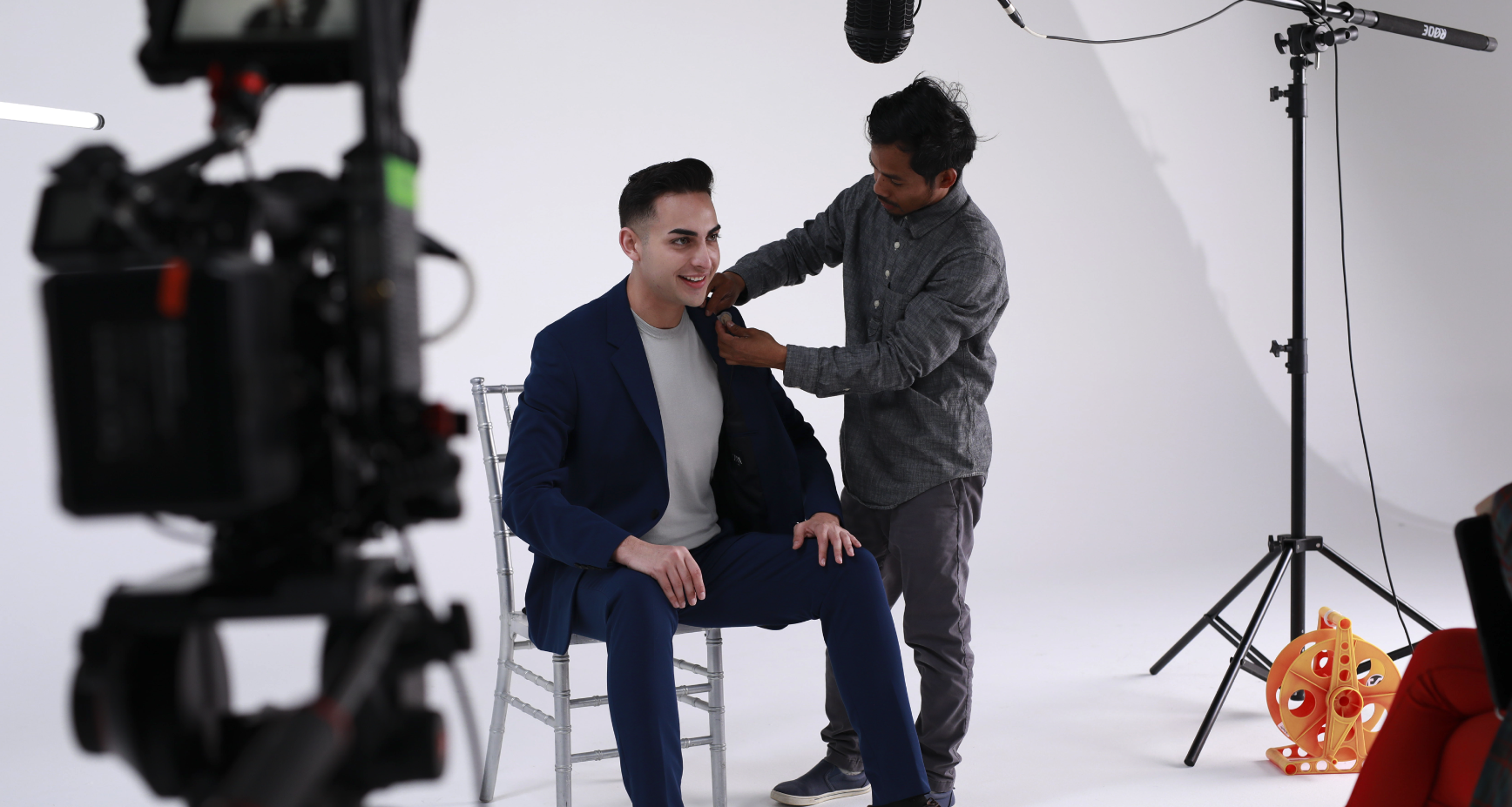 Behind the scenes — sound technician adjusting a lavalier microphone on an interview subject seated on a studio cyclorama